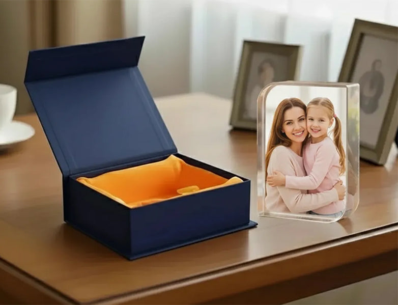 Blue gift box with orange interior on a wooden surface, next to a glass photo block with a family photo.