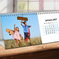 Desk Calendar with children playing on a grassy field, showing January 2027, on a wooden surface.