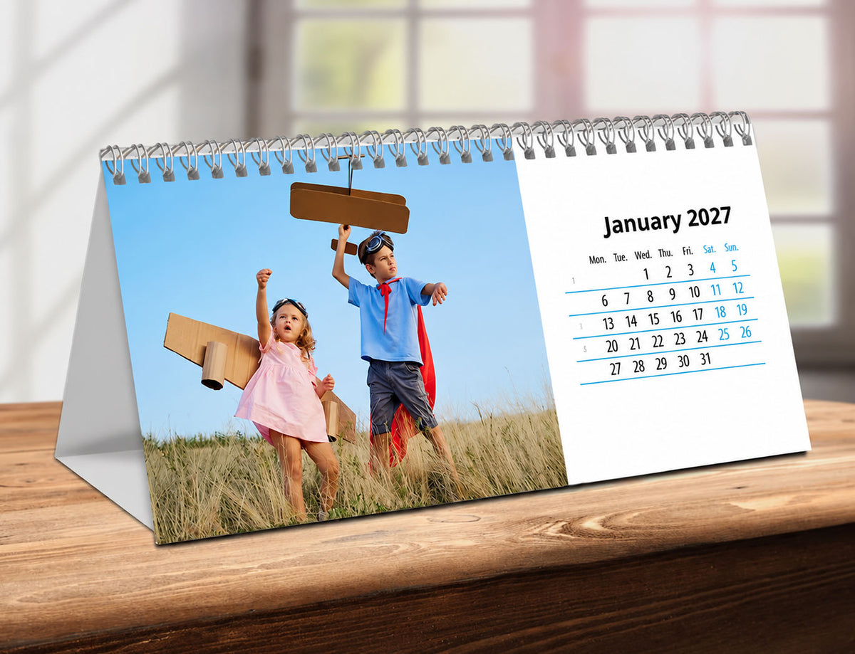 Desk Calendar with children playing on a grassy field, showing January 2027, on a wooden surface.