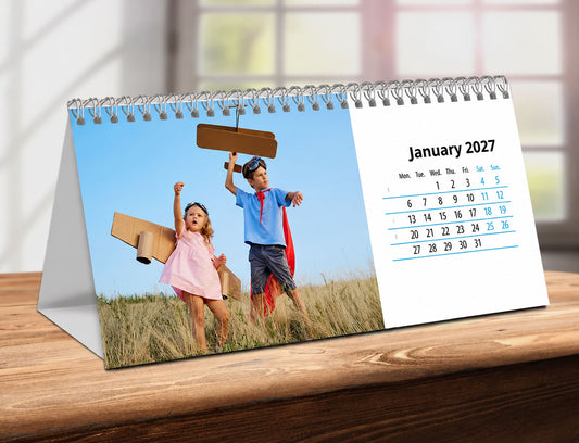 Desk Calendar with children playing on a grassy field, showing January 2027, on a wooden surface.