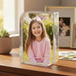 Clear photo frame with a young girl's smiling photo on a wooden surface.