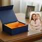 Blue gift box with orange interior on a wooden surface, next to a glass photo frame with a family photo.